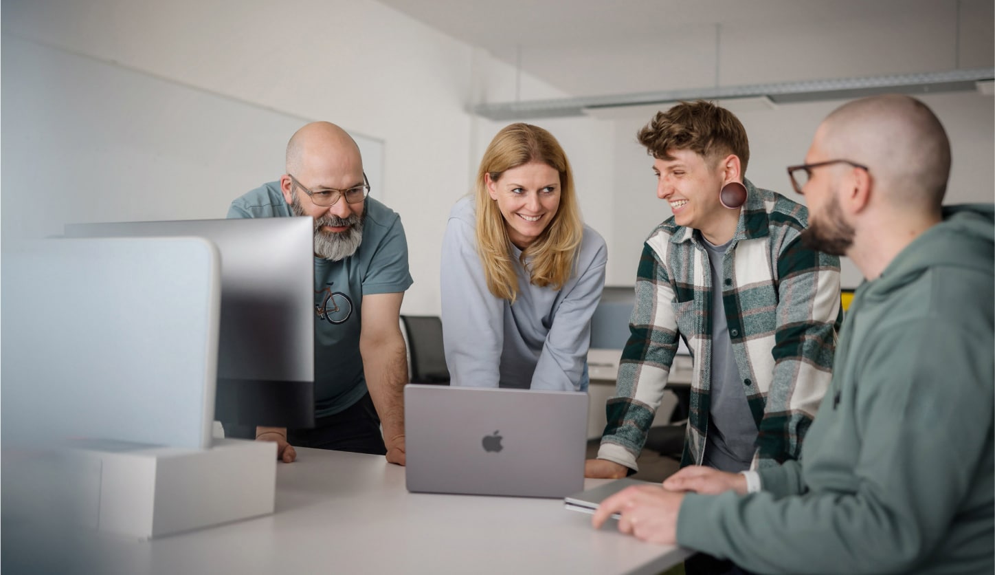 Vierköpfiges Produktentwicklungsteam arbeitet kollaborativ an einem Projekt mit MacBooks – moderne Teamarbeit im digitalen Entwicklungsumfeld.